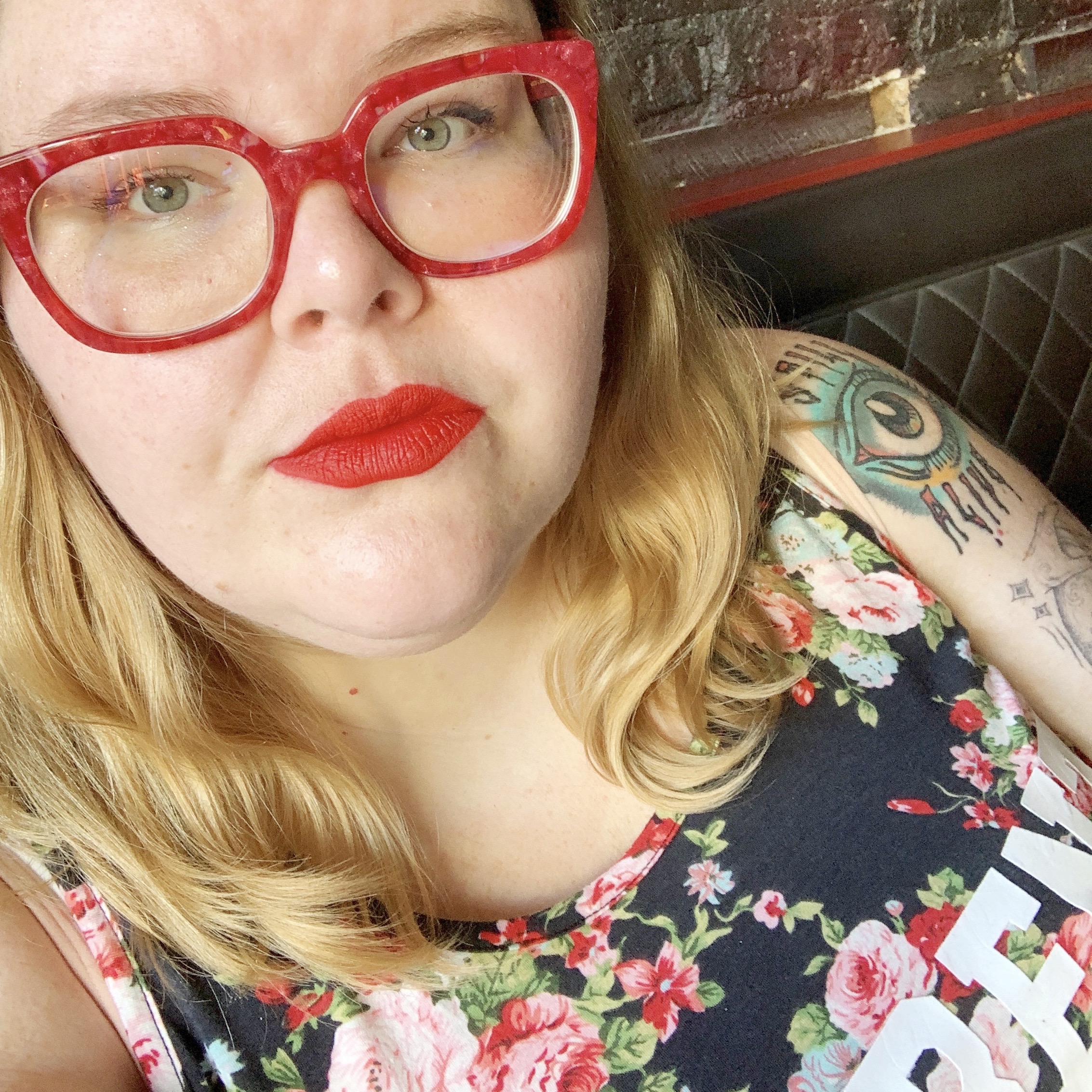 ash in red glasses and red lipstick and a floral top