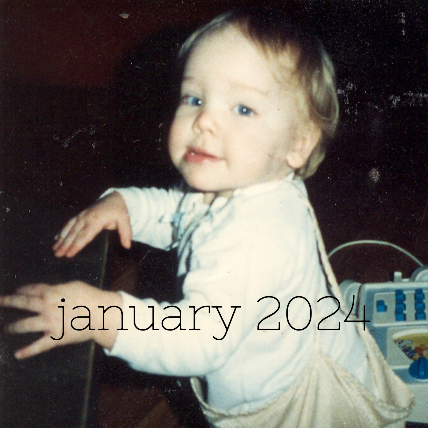 a square image of a small pale toddler standing with their hands on piano keys with the text january 2024 toward the bottom center