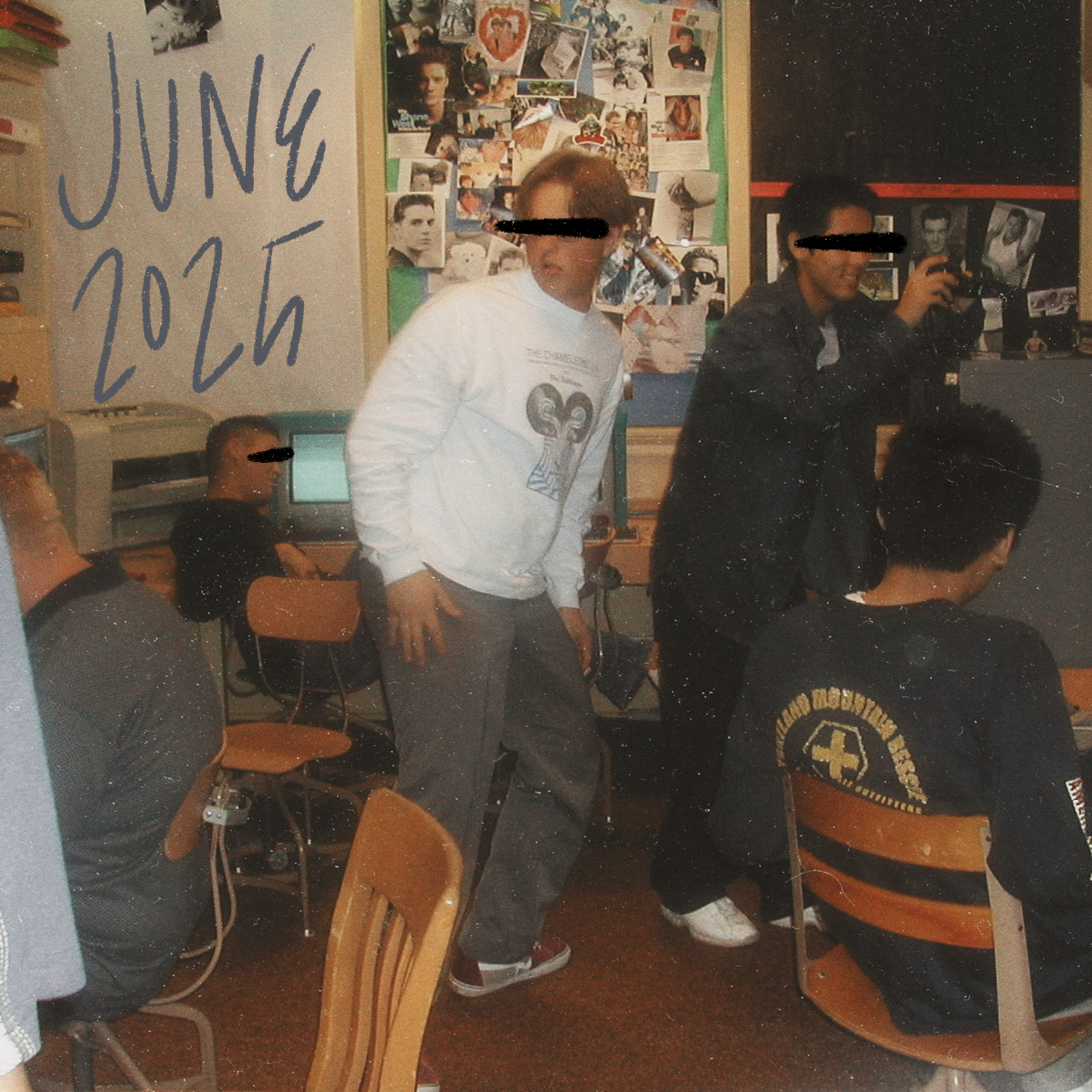 a square image of several teenage boys in a journalism computer lab, three of them are seated and ostensibly working at computers, one is standing with his head turned back to look at something to his right, another is standing and taking a picture with a digital camera, june 2025 is handwritten in blue on the top right, the image was taken sometime in 2001 or 2002