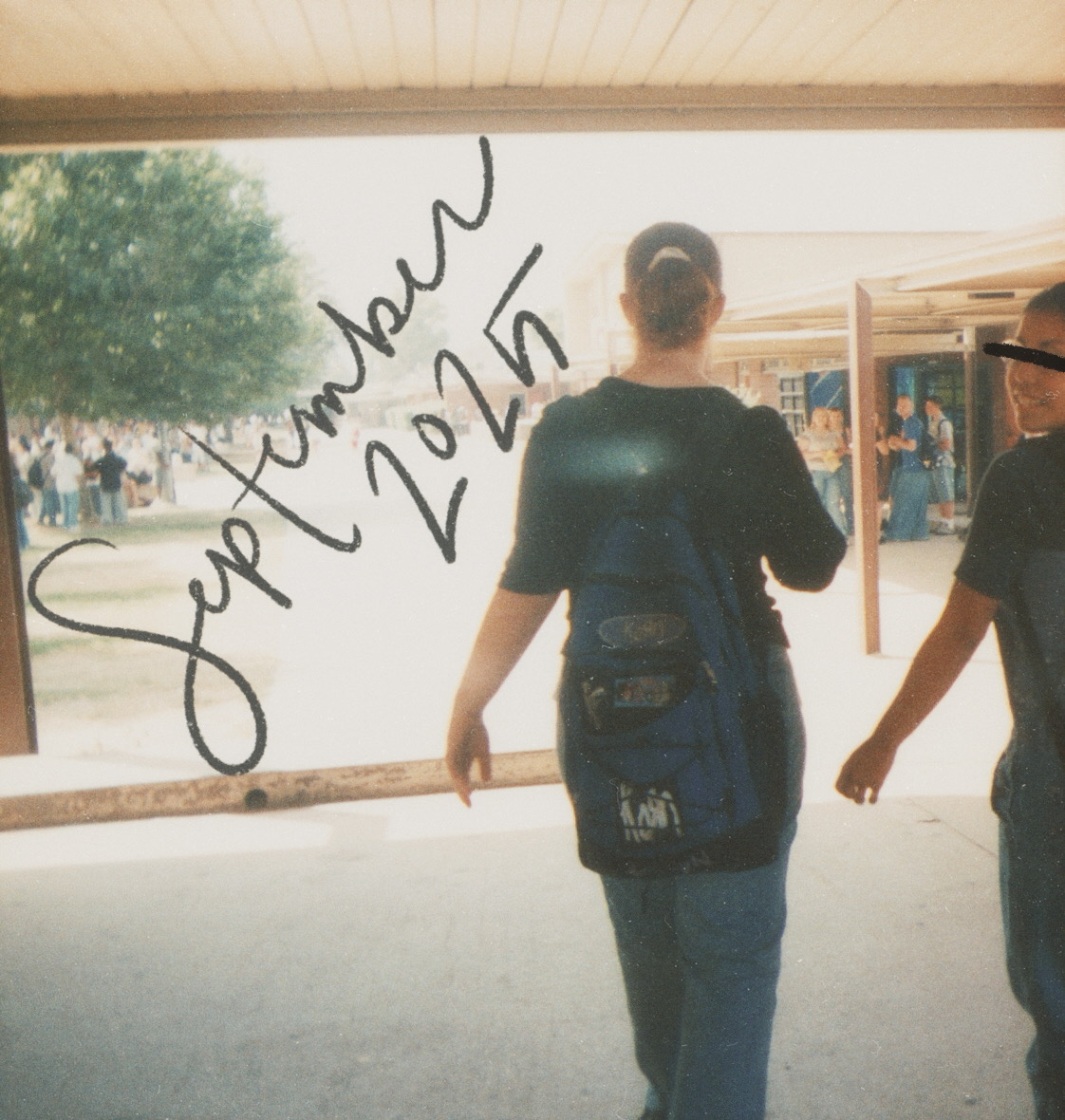 a square image of two people walking through a school hallway, one is turned back to smile at the camera, both are wearing backpacks, there are two large groups of people in the background to both the right and left, september 2025 is written in dark denim blue cursive, the picture was likely taken 1999 or 2000