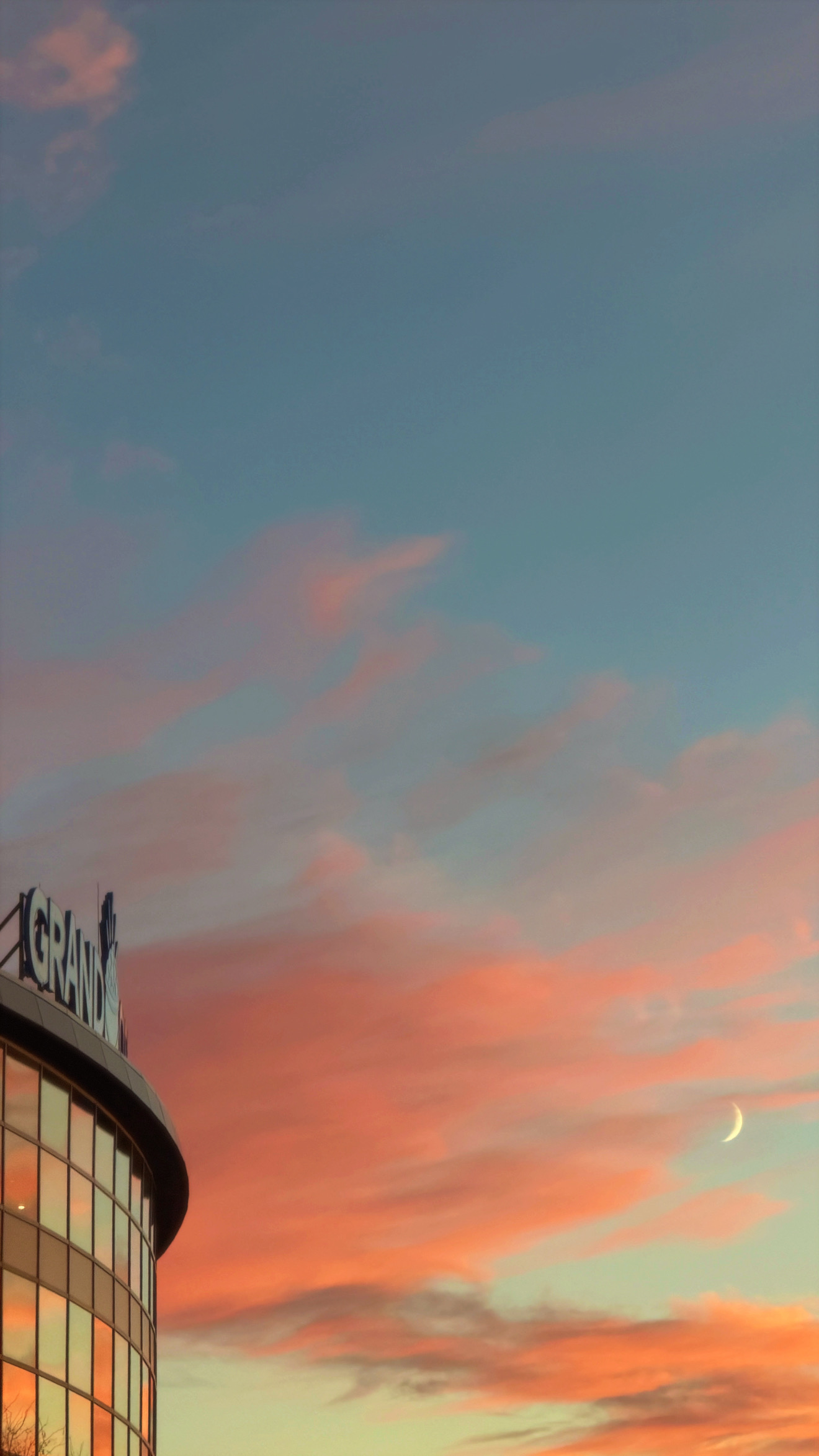 the glass front of grand casino arena to the left reflecting a pink and orange sunset with a crescent moon to the right