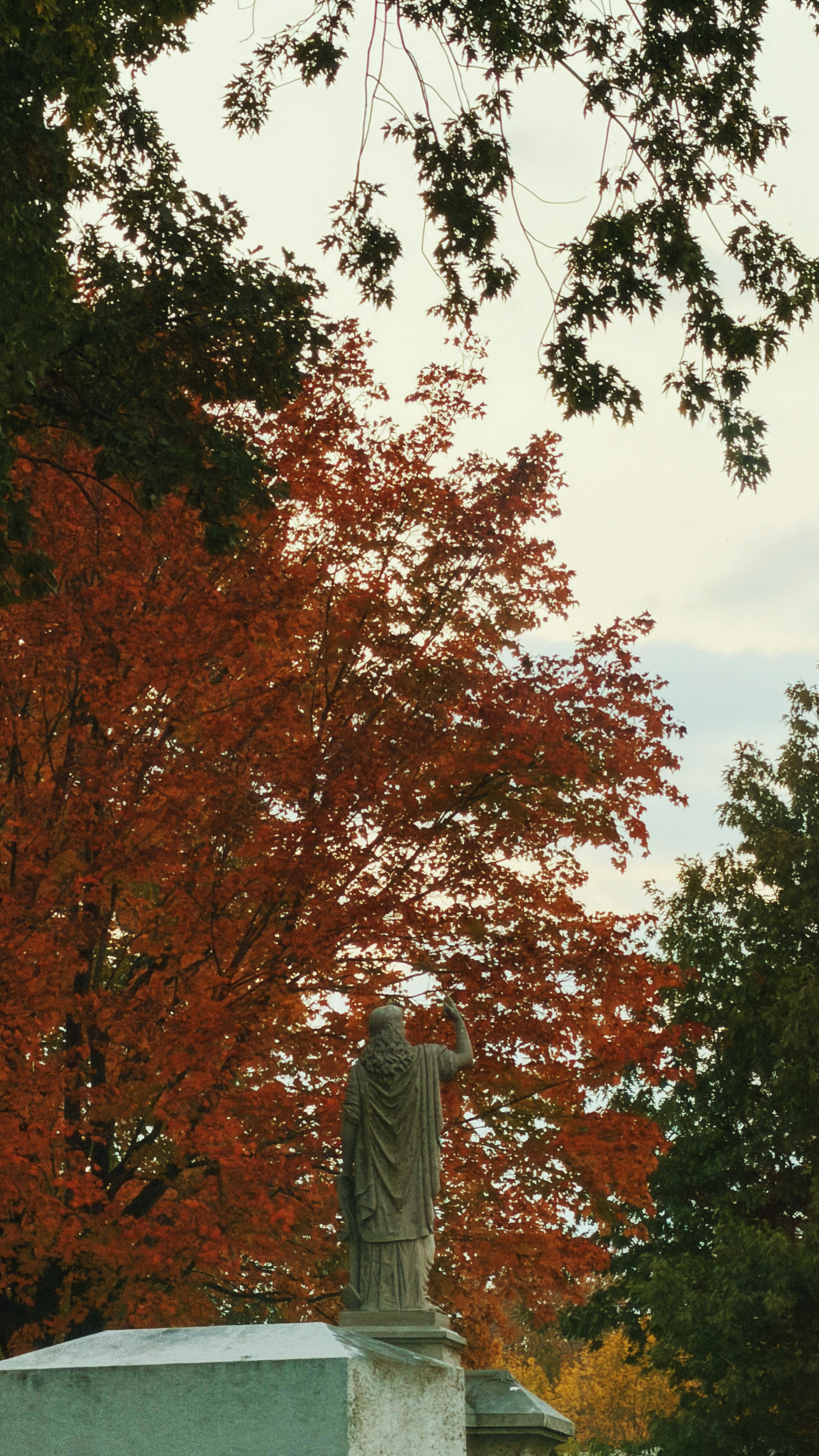 the back side of a funerary statue in lakewood cemetery with orange fall trees behind it